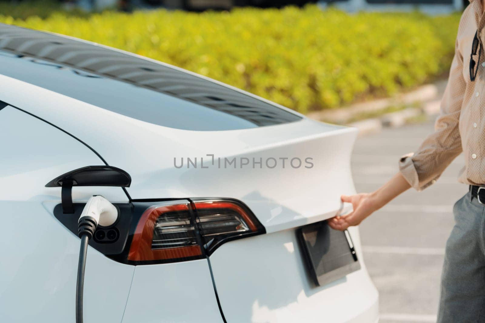 Young woman open trunk while EV car recharging battery. Expedient by biancoblue