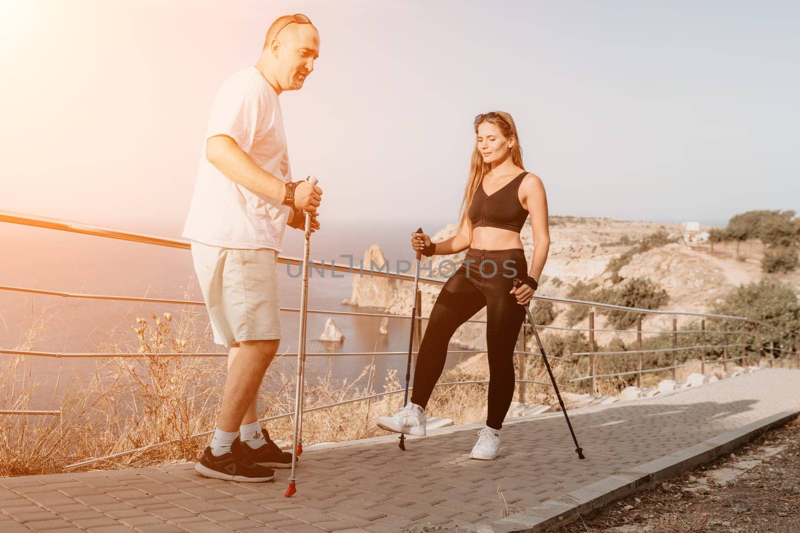 Happy Middle aged couple or friends practicing nordic walking in park near sea. Mature couple with trekking poles walking, practicing Nordic walking outdoors. Aging youthfully and sport concept.