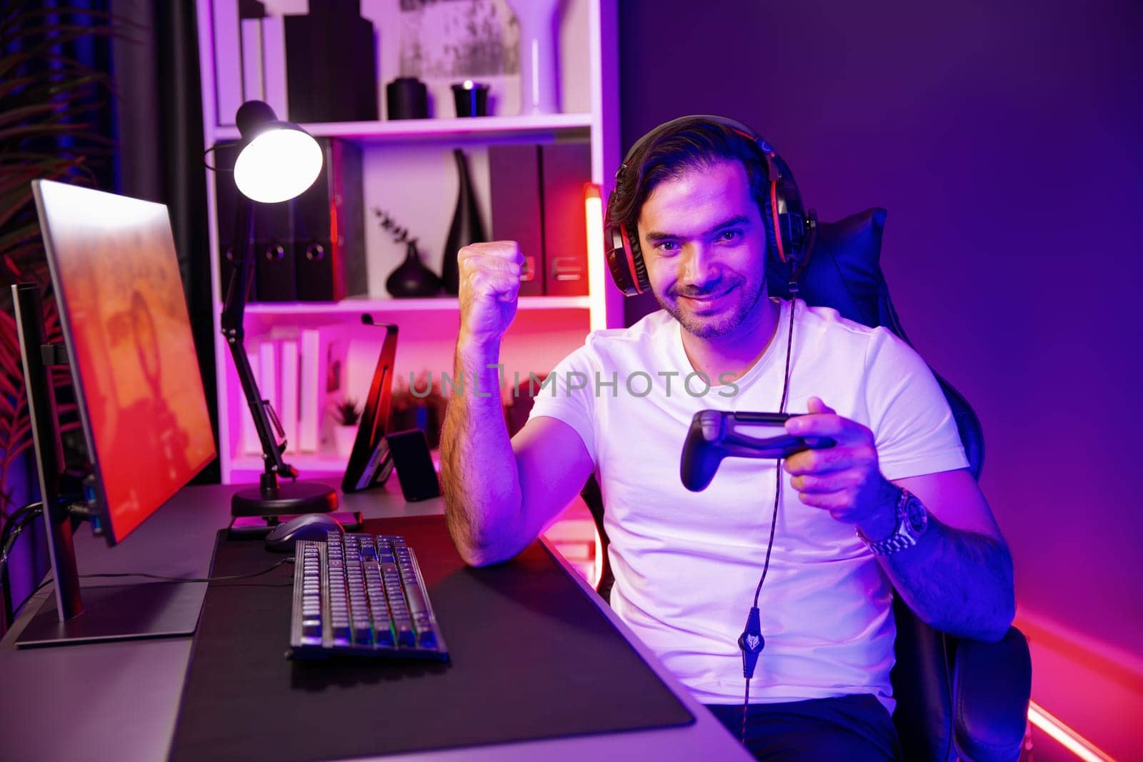 Smart gaming streamer with joystick player looking at camera, playing battle team shooting gun background at warship on pc screen at side view, wearing headset at digital neon light studio. Surmise.