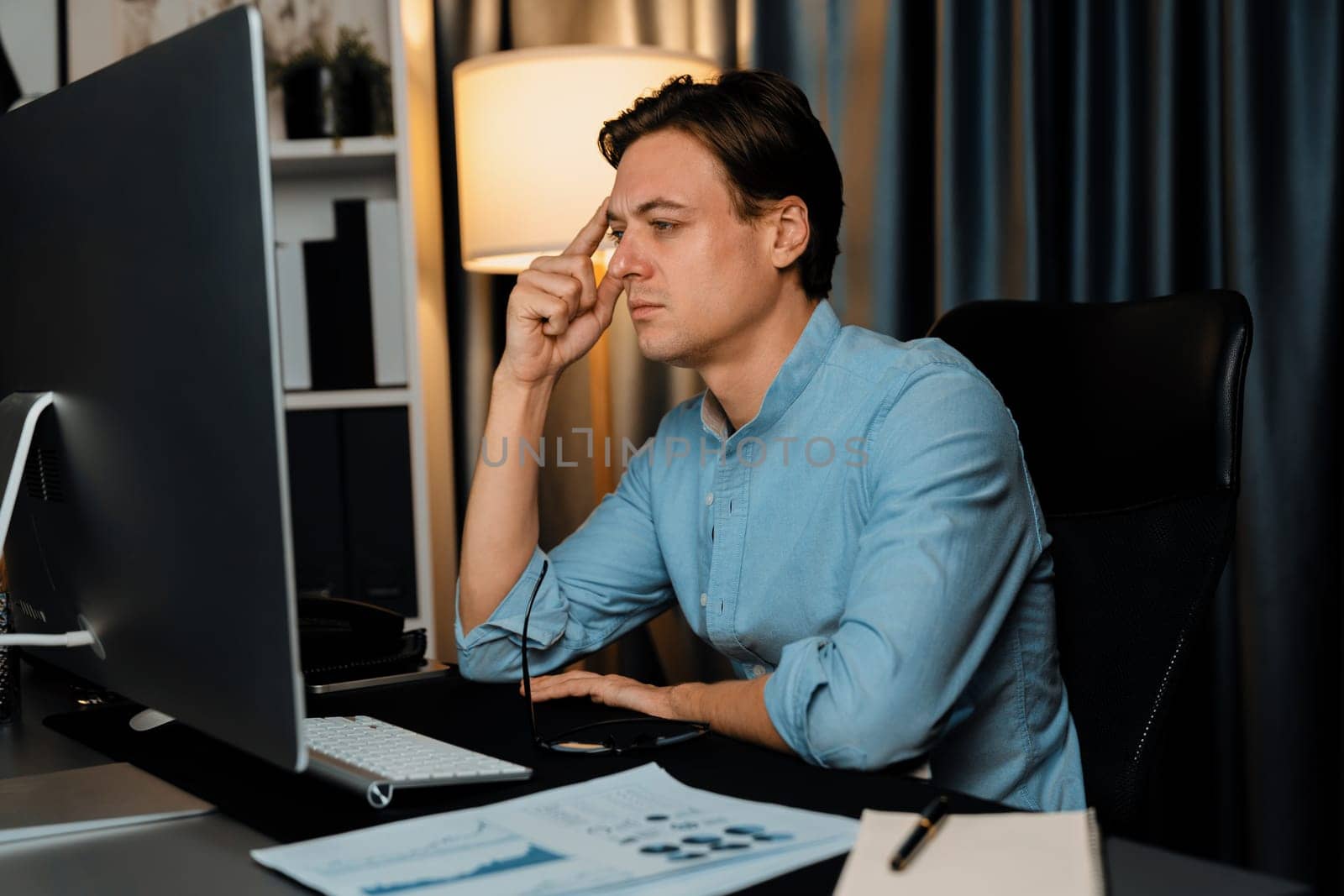 Thinking of stressful financial analyst researching on business paragraph on pc screen with dynamic database marketing analysis planning monthly report at modern home office at night time. Pecuniary.