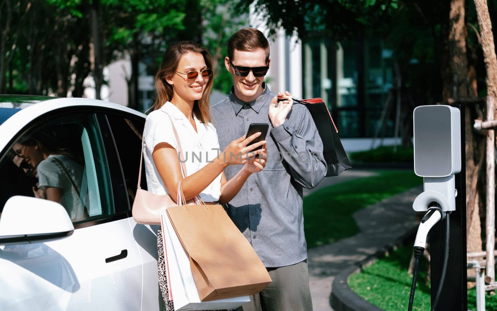 Young couple travel with EV electric car in green sustainable city innards by biancoblue