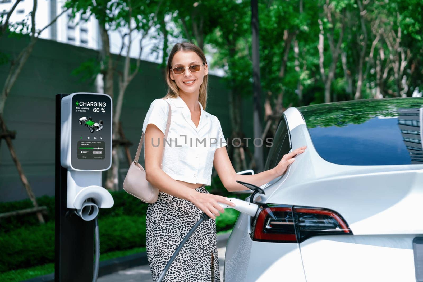 Young woman travel with EV electric car charging in green sustainable city outdoor garden in summer. Urban sustainability lifestyle by green clean rechargeable energy of electric BEV vehicle innards