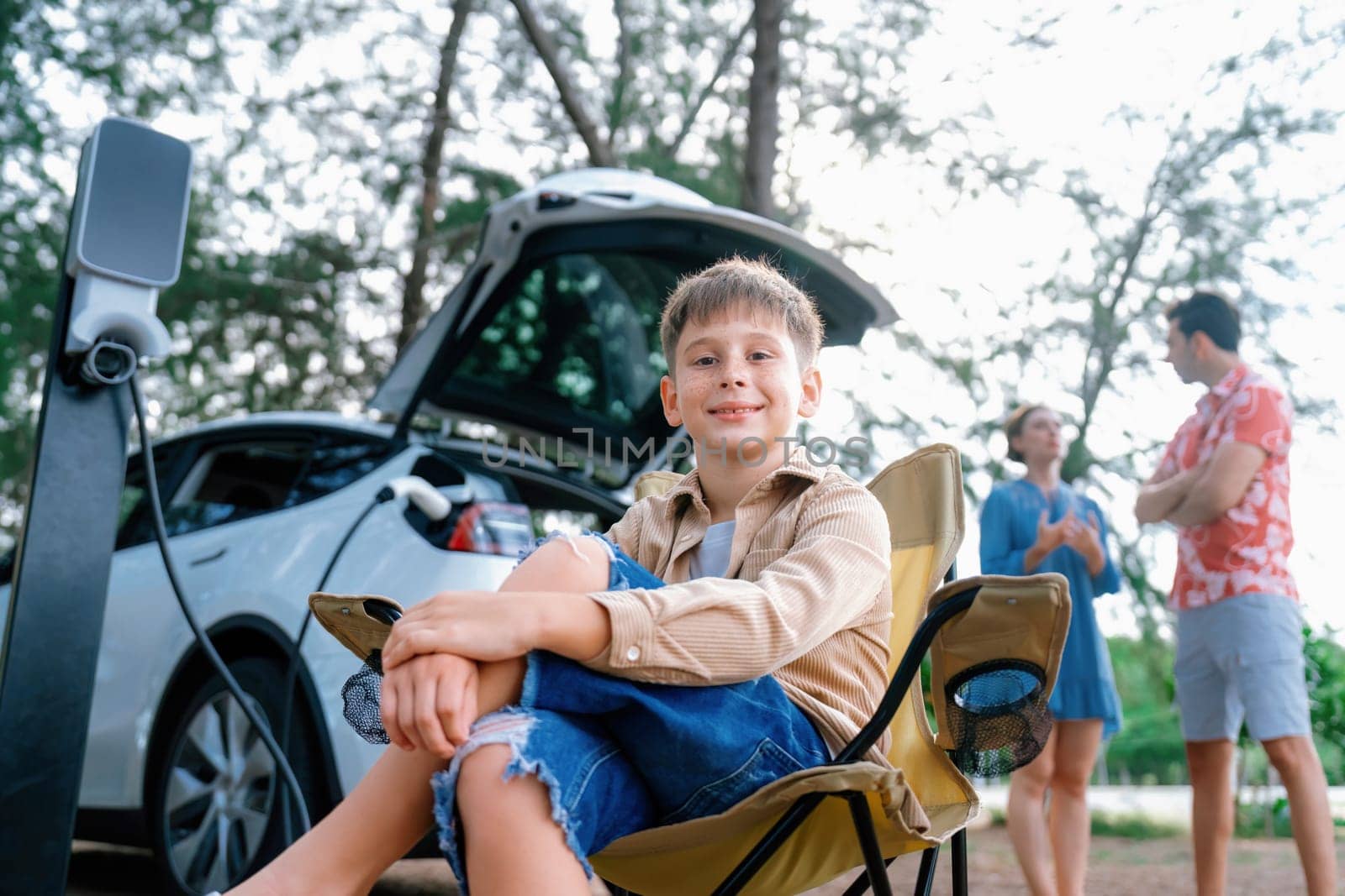 Little boy portrait sitting on camping chair with family. Perpetual by biancoblue