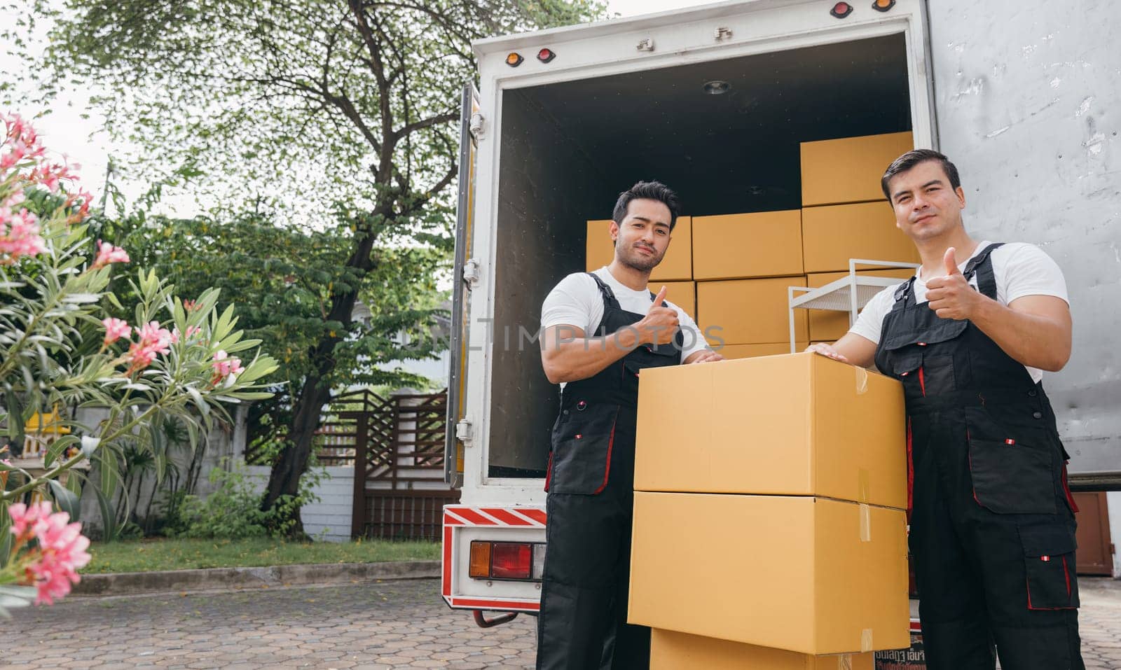 Efficient workers in uniform unload boxes from the moving truck ensuring a smooth delivery for customer relocation. The team dedication guarantees happiness. Moving Day by Sorapop