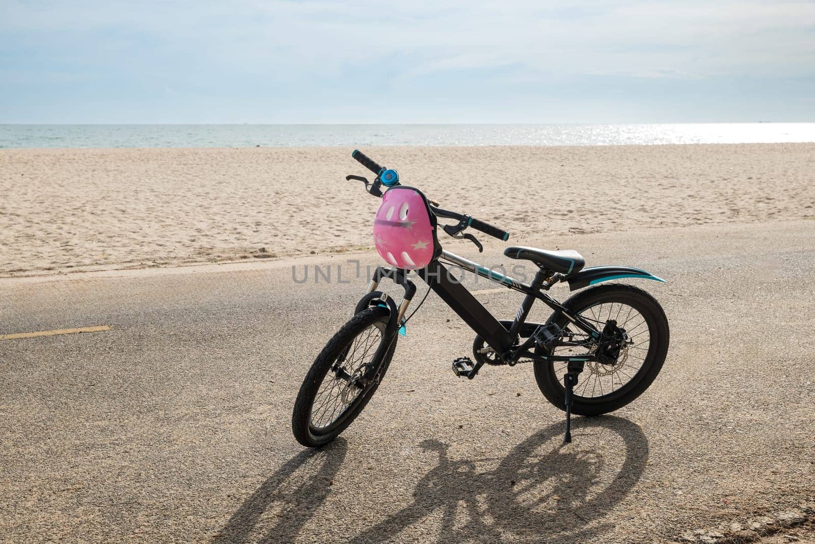 A tranquil summer day unfolds with a child's bicycle on a sandy beach capturing the carefree spirit of tourism where relaxation and sport meet against the backdrop of the sea and clear skies.