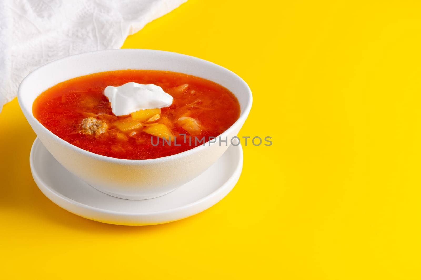 Red borscht in bowl on a yellow background, traditional dish that is cooked with broth. Copy space.