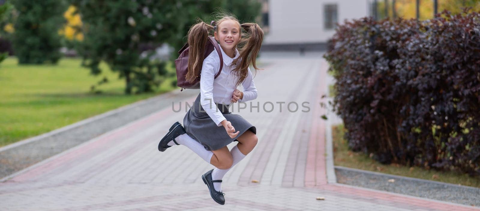 Happy caucasian girl in uniform and with a backpack jumping outdoors after school