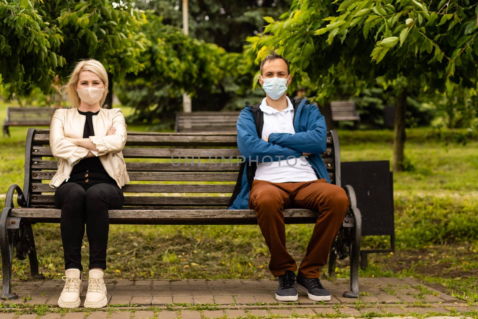 Woman and man in social distancing sitting on bench in park by Andelov13