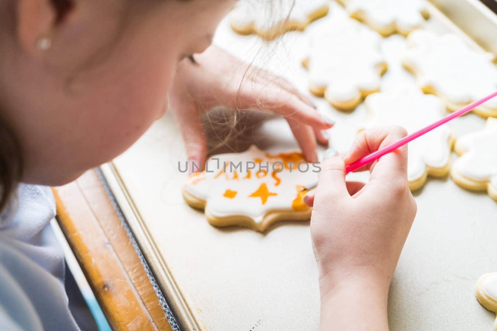 A heartwarming scene of a little girl carefully writing 'Sorry' on sugar cookies with food coloring, the cookies beautifully flooded with white royal icing.