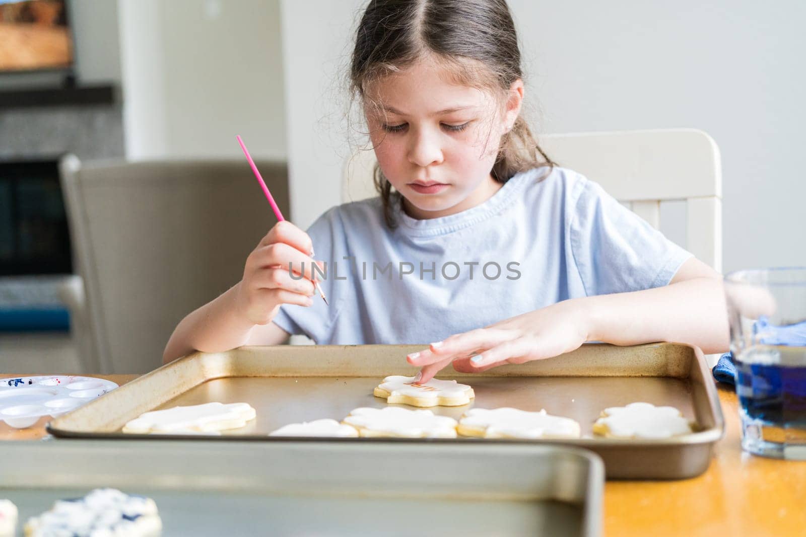 A heartwarming scene of a little girl carefully writing 'Sorry' on sugar cookies with food coloring, the cookies beautifully flooded with white royal icing.