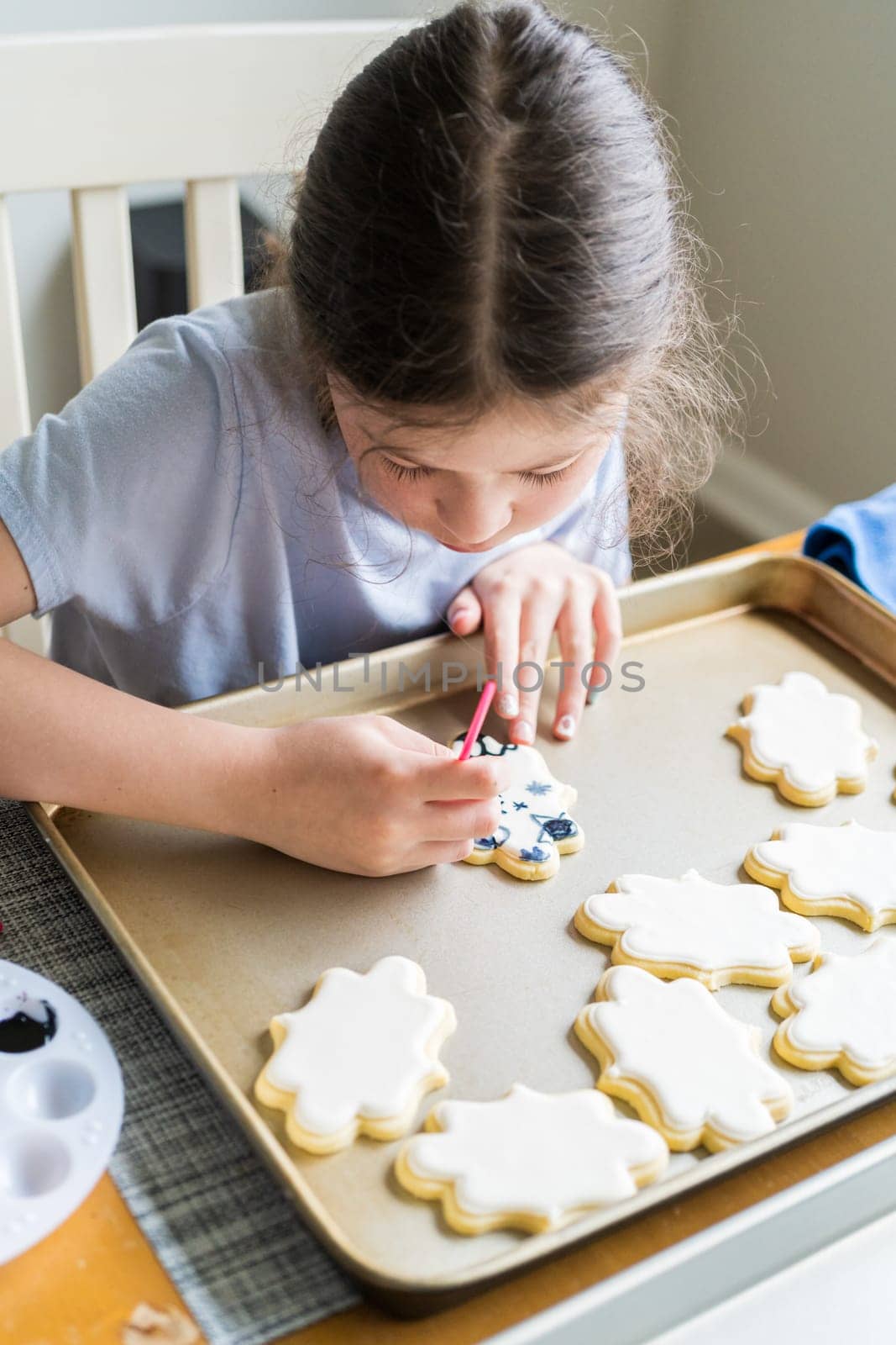 A heartwarming scene of a little girl carefully writing 'Sorry' on sugar cookies with food coloring, the cookies beautifully flooded with white royal icing.