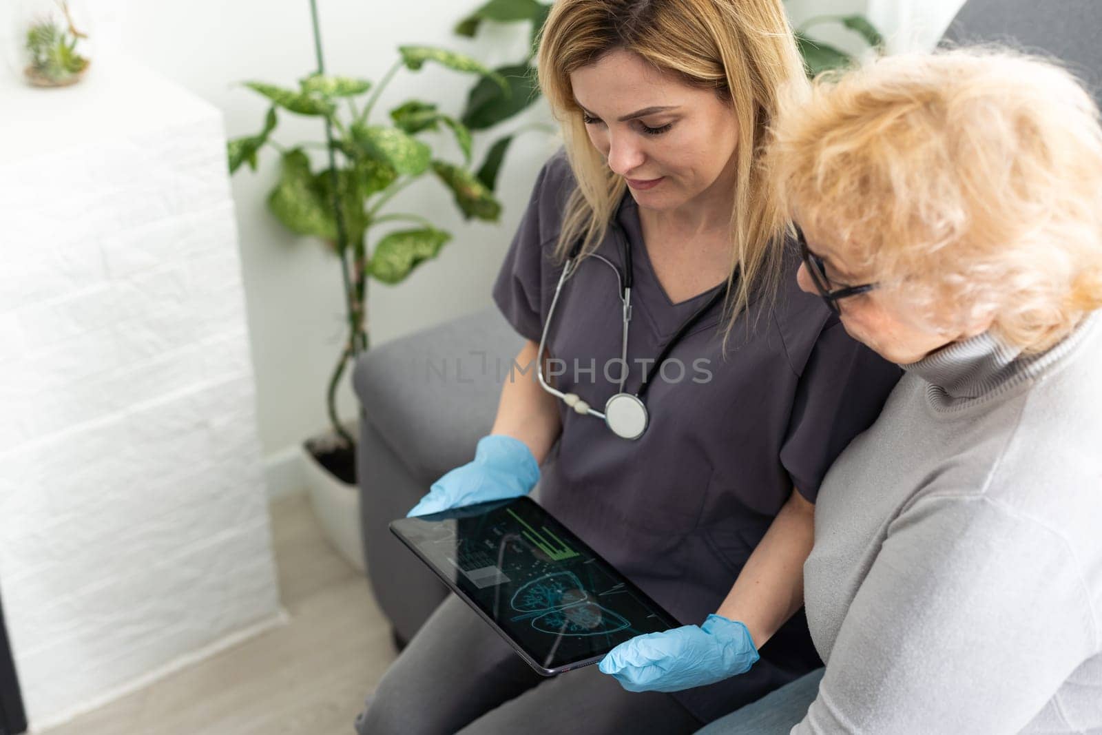 Doctor or nurse caregiver holding a tablet computer with senior woman at home or nursing home by Andelov13