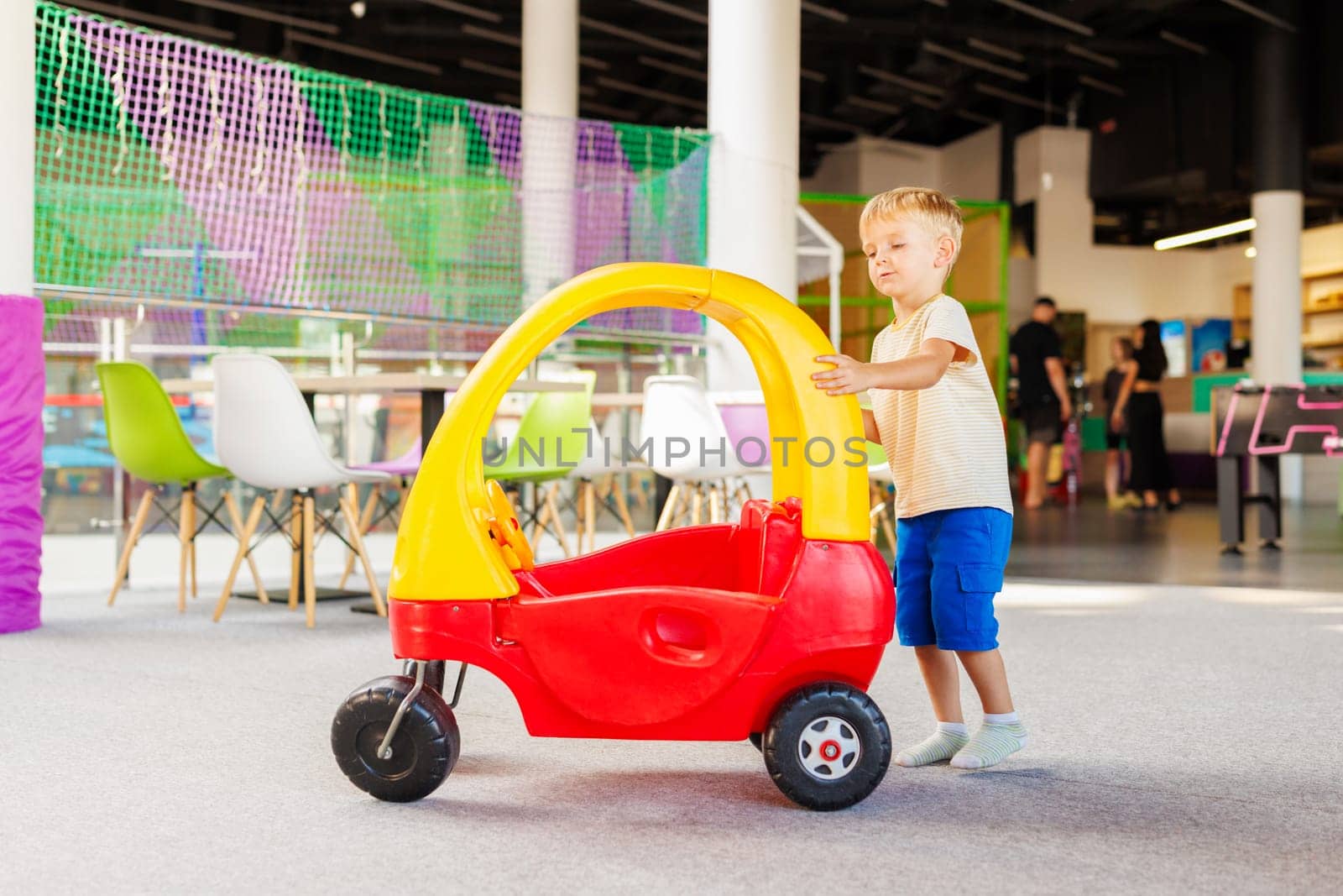 A young child enjoys playtime, pushing a colorful toy car in a vibrant indoor play area.