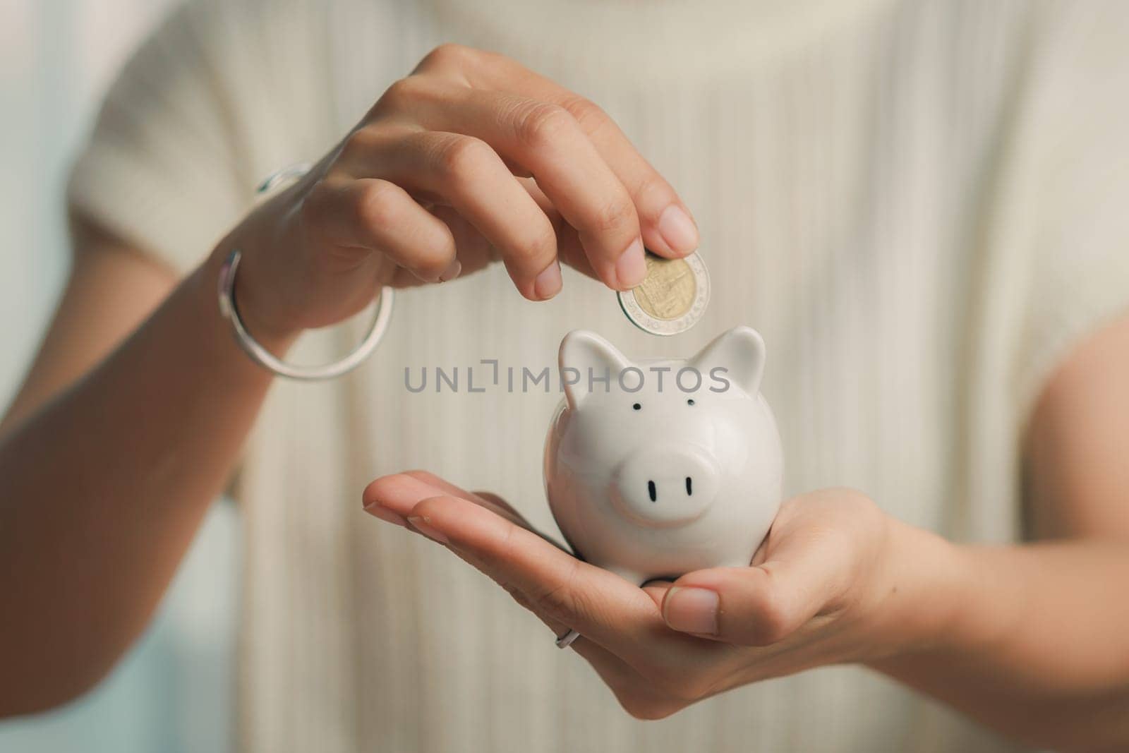 Person deposits a coin into a piggy bank by iamnoonmai
