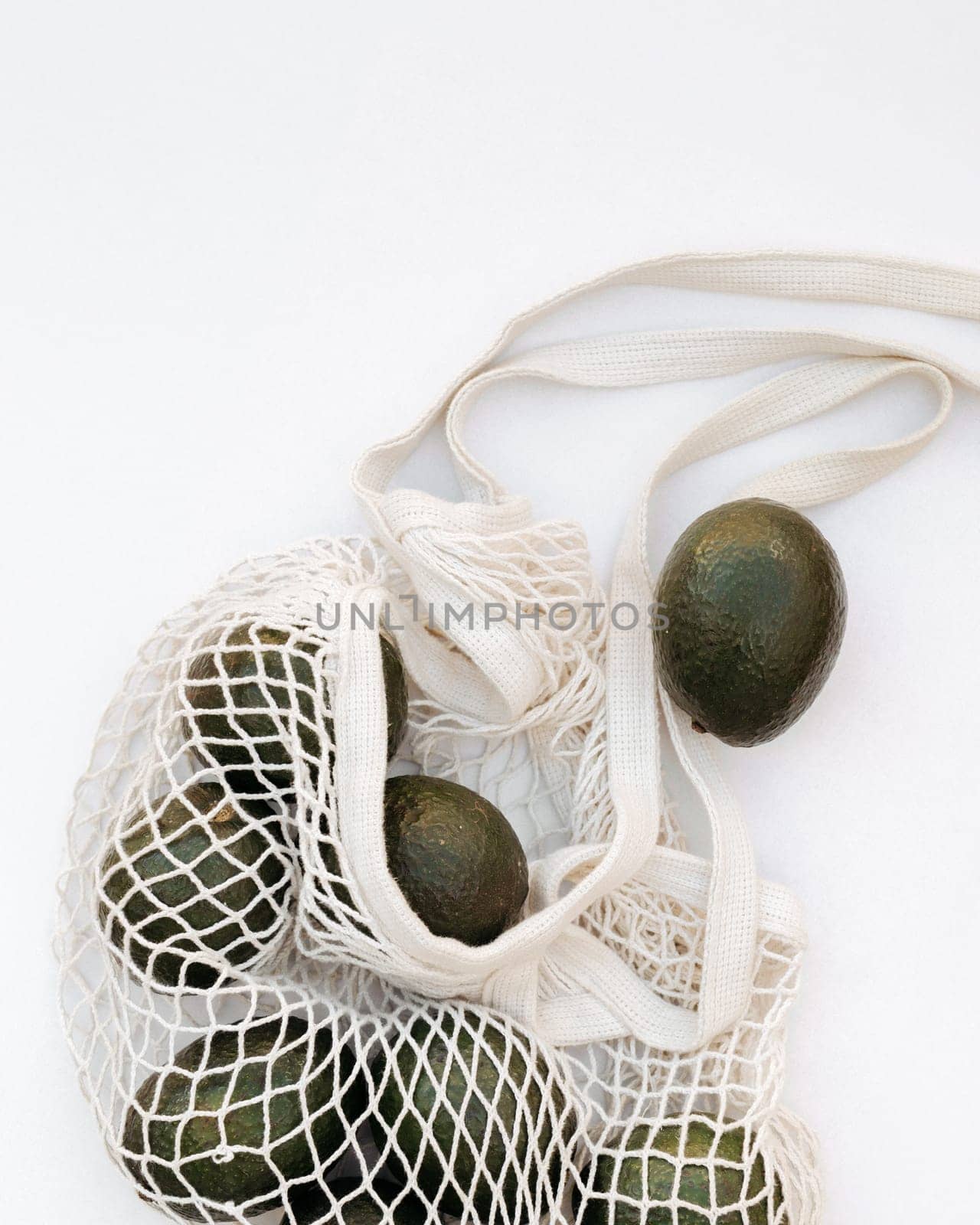 Avocados spilling from an eco-friendly net bag on a white background, concept of sustainable shopping