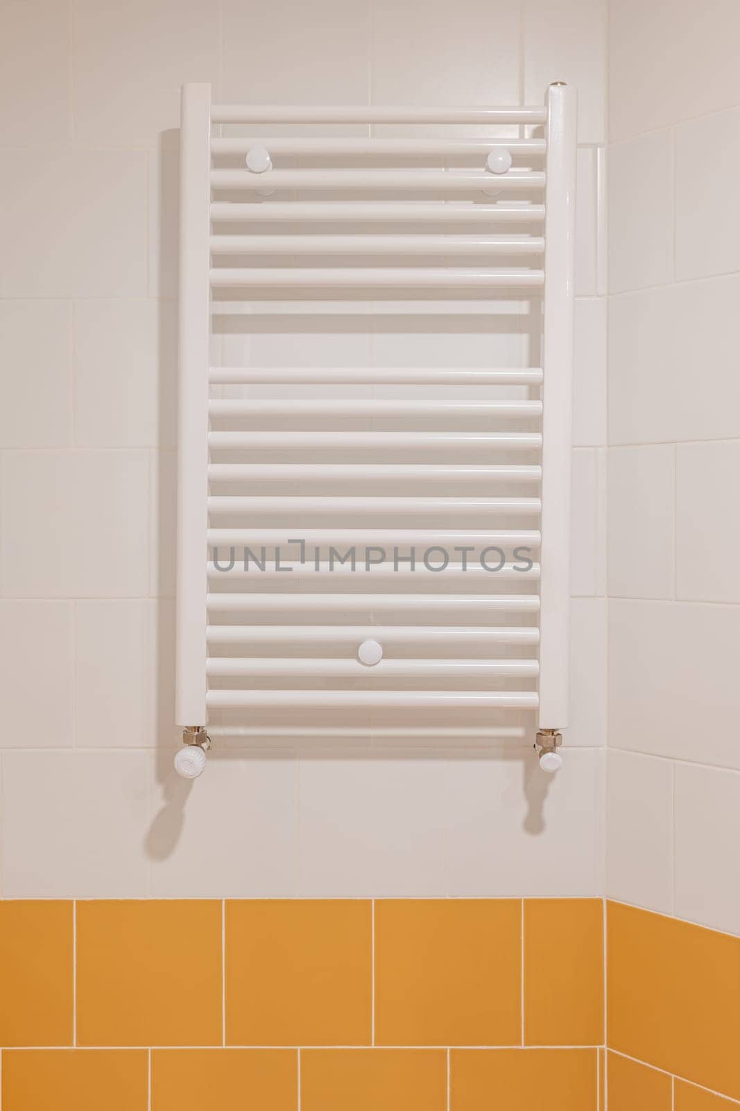 White bathroom radiator mounted on a half yellow, half white tiled wall