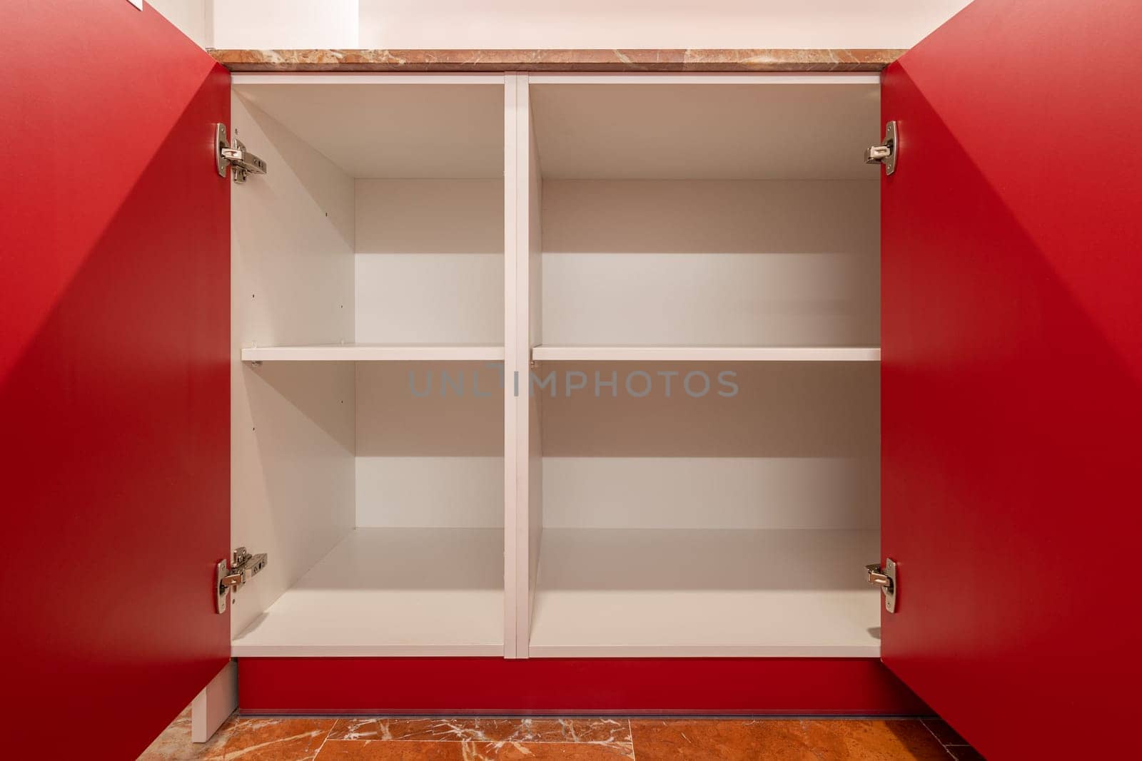 Bright red open cupboard with empty white shelves and a terracotta tiled floor by apavlin