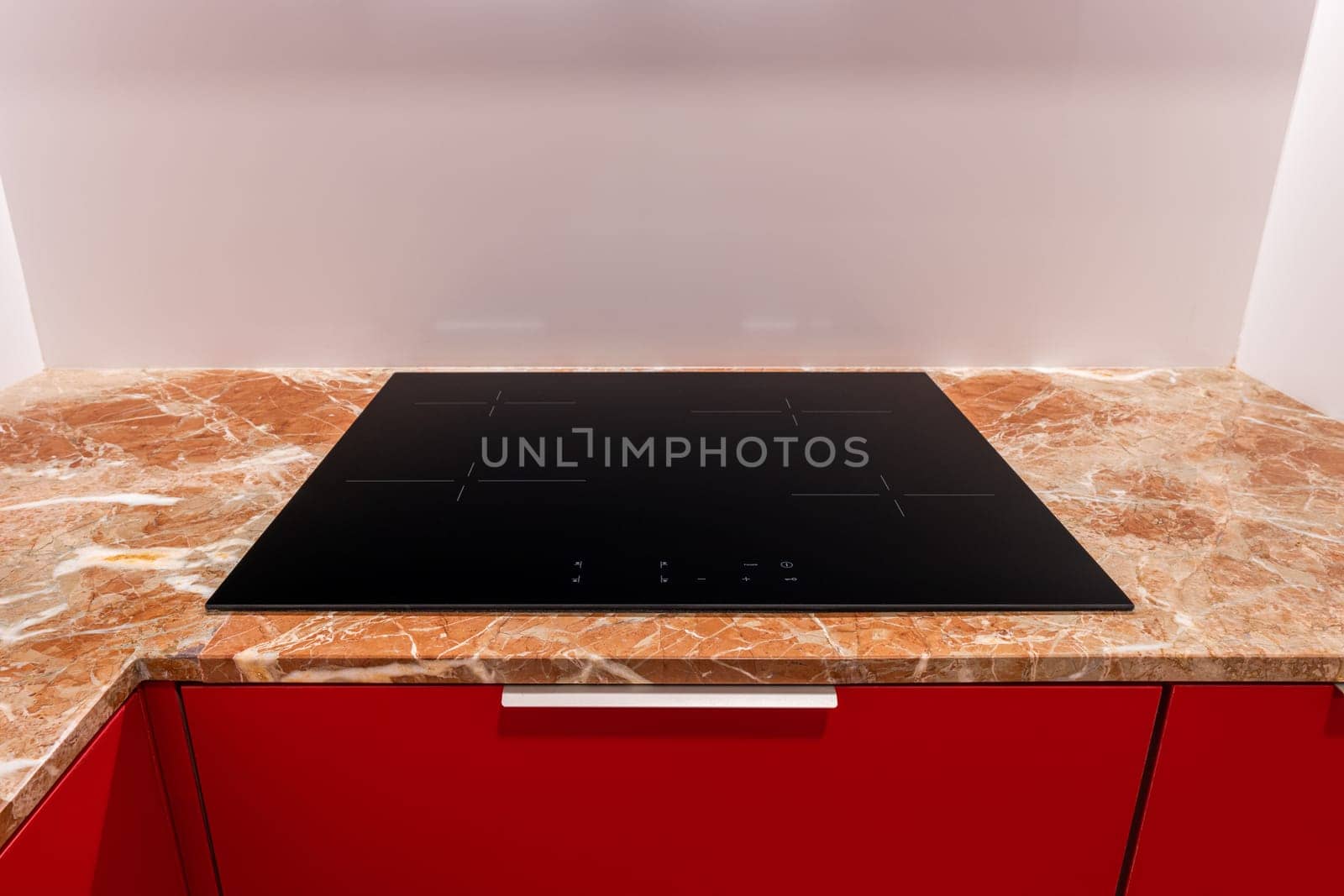 Modern induction cooktop on a marble countertop with red cabinets by apavlin