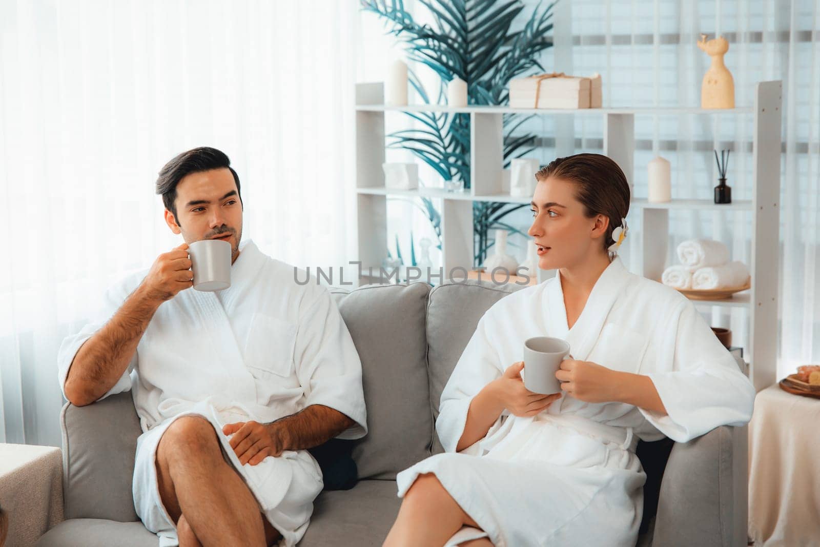 Beauty or body treatment spa salon vacation lifestyle concept with couple wearing bathrobe relaxing with drinks in luxurious hotel spa or resort room. Vacation and leisure relaxation. Quiescent