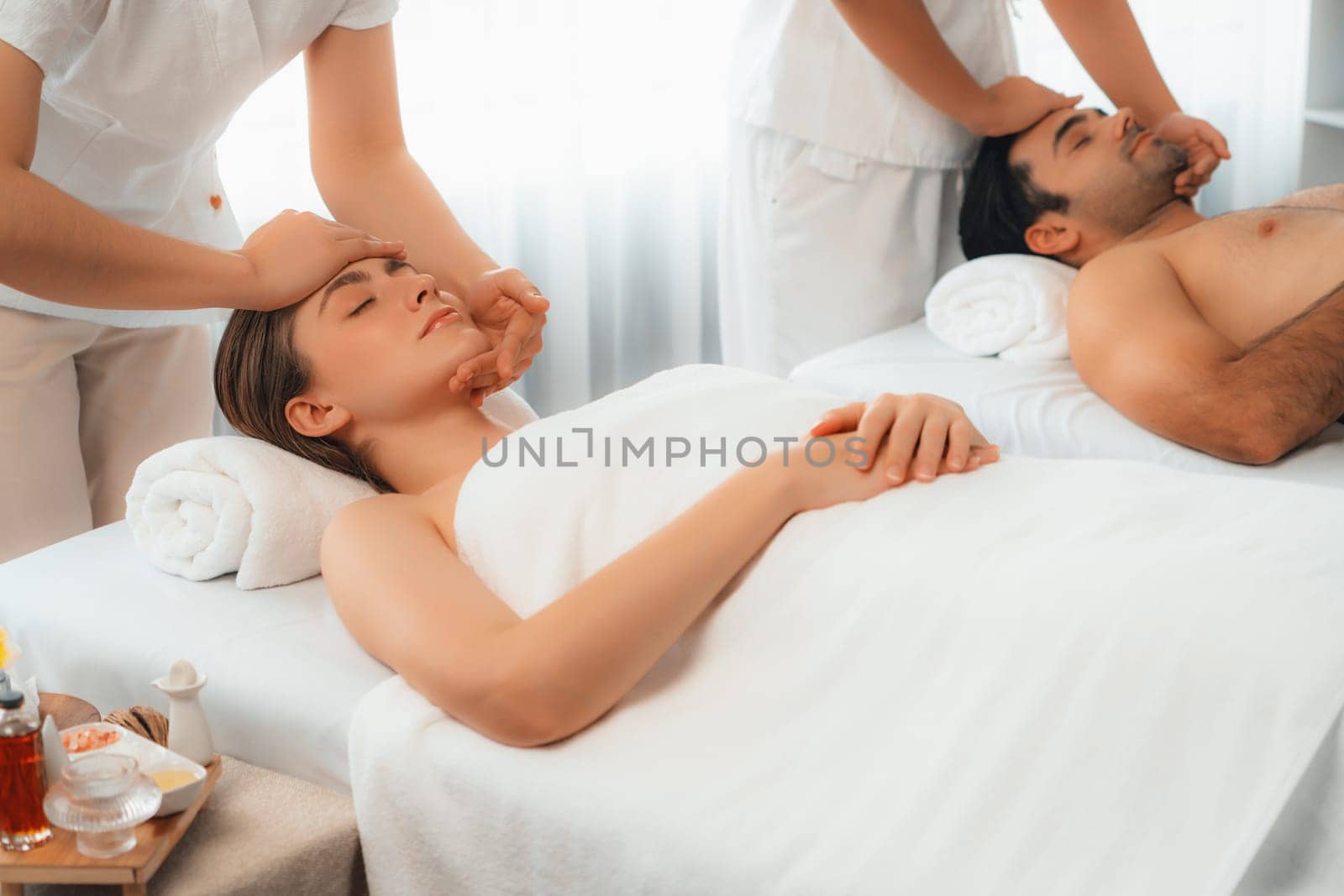 Caucasian couple enjoying relaxing anti-stress head massage and pampering facial beauty skin recreation leisure in dayspa modern light ambient at luxury resort or hotel spa salon. Quiescent