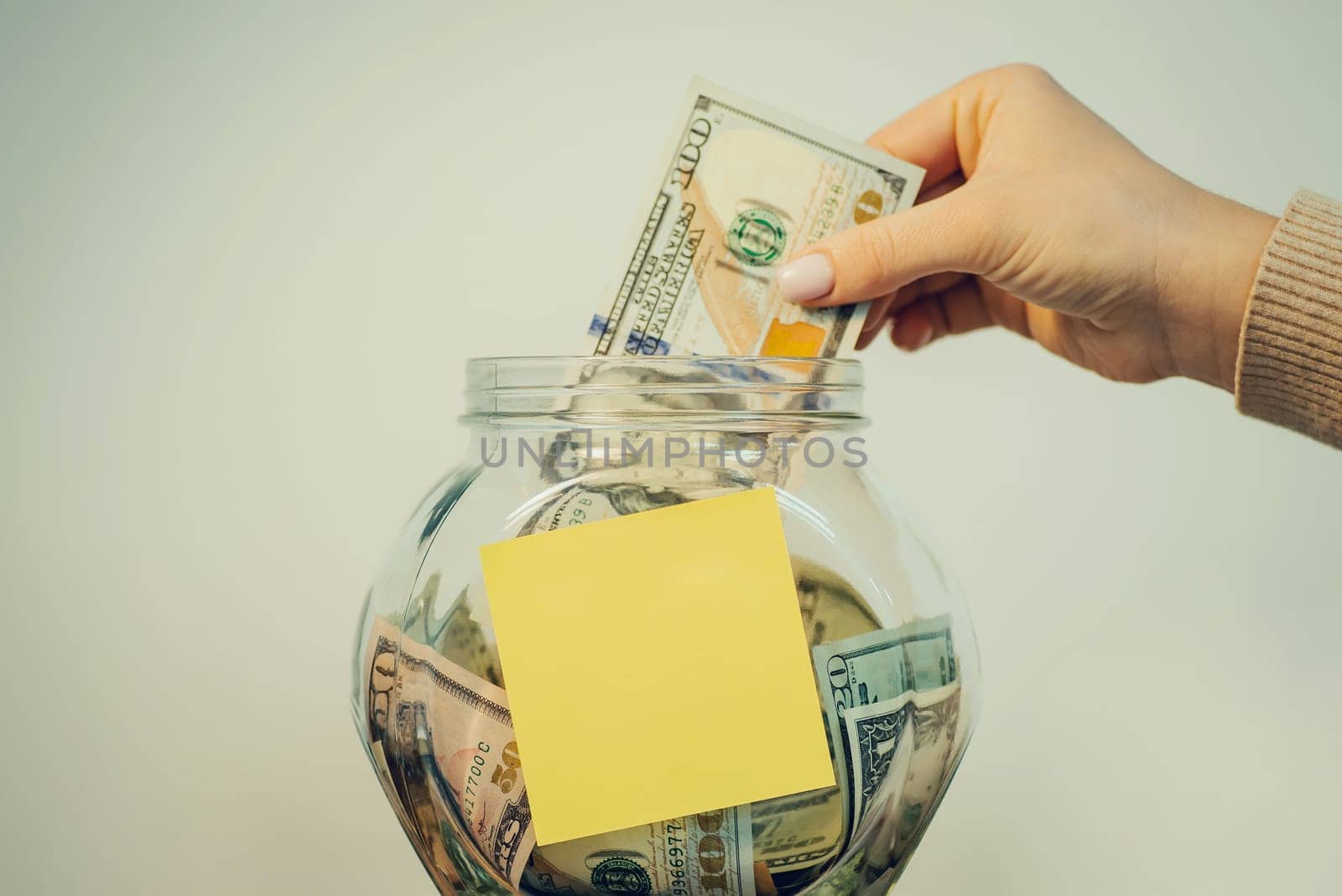 Female hand putting one hundred dollar bill into the glass jar by VitaliiPetrushenko