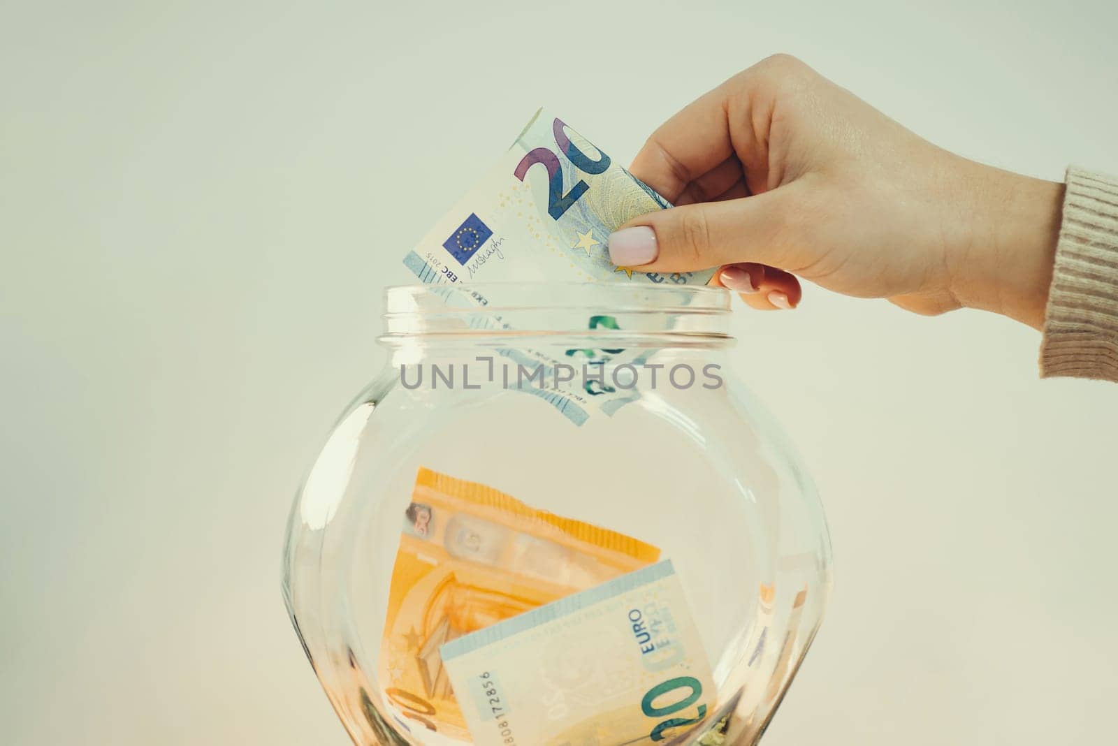 Woman putting 20 euro bill in glass jar by VitaliiPetrushenko