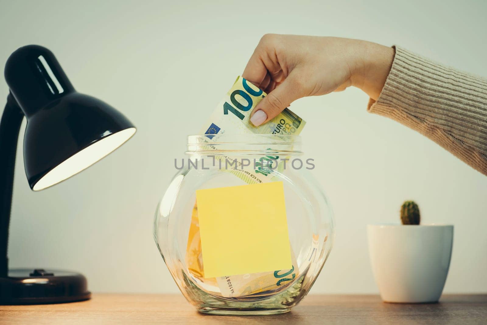 Female putting one hundred euro banknote to glass jar, toned by VitaliiPetrushenko