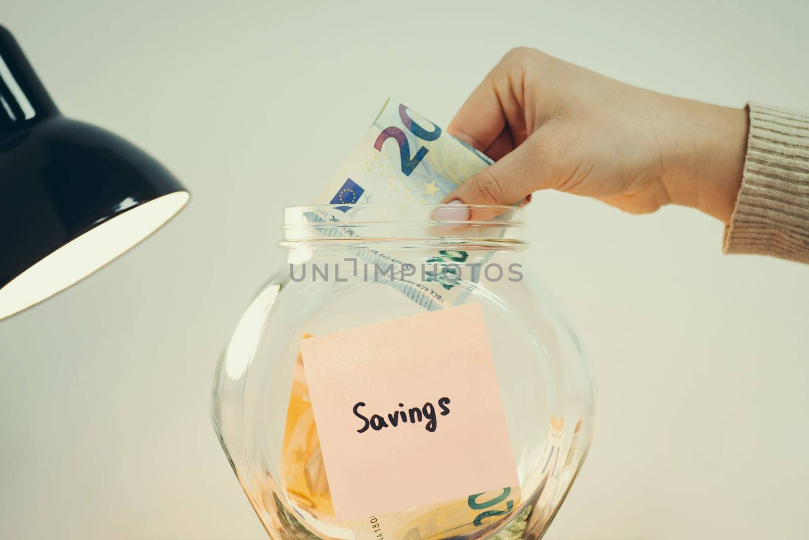 Person putting 20 euro banknote into the glass jar