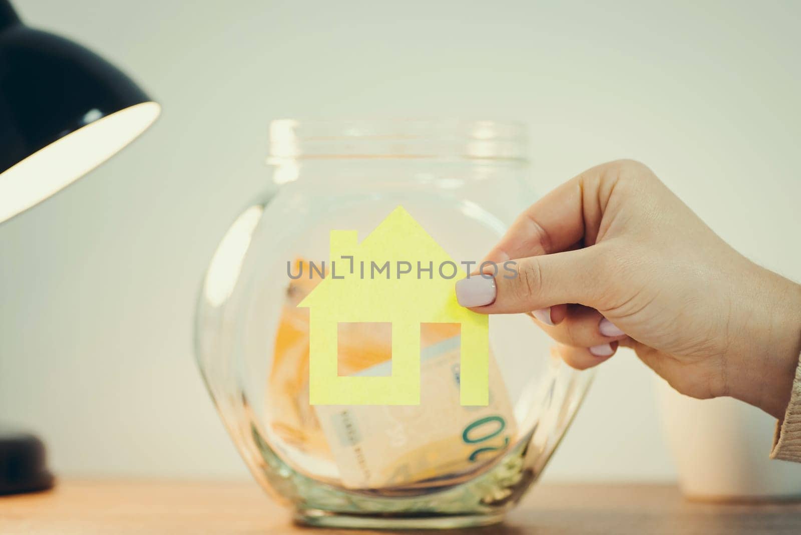 Putting house symbol on glass savings jar on the table, toned by VitaliiPetrushenko