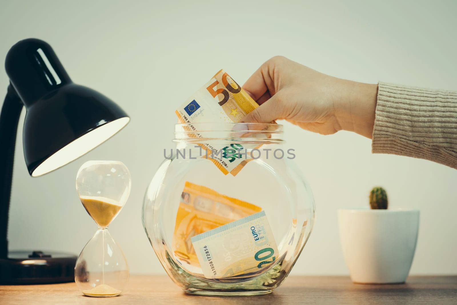 Person putting 50 euro banknote into the glass jar on the table