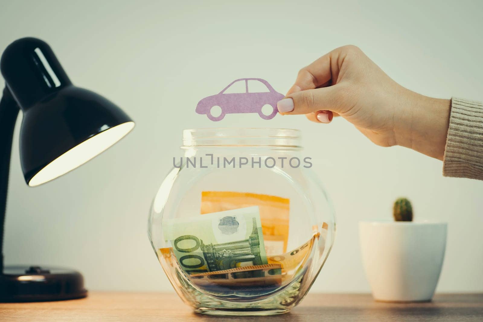 Female holding paper car above glass bank with some euro banknotes in it, toned image