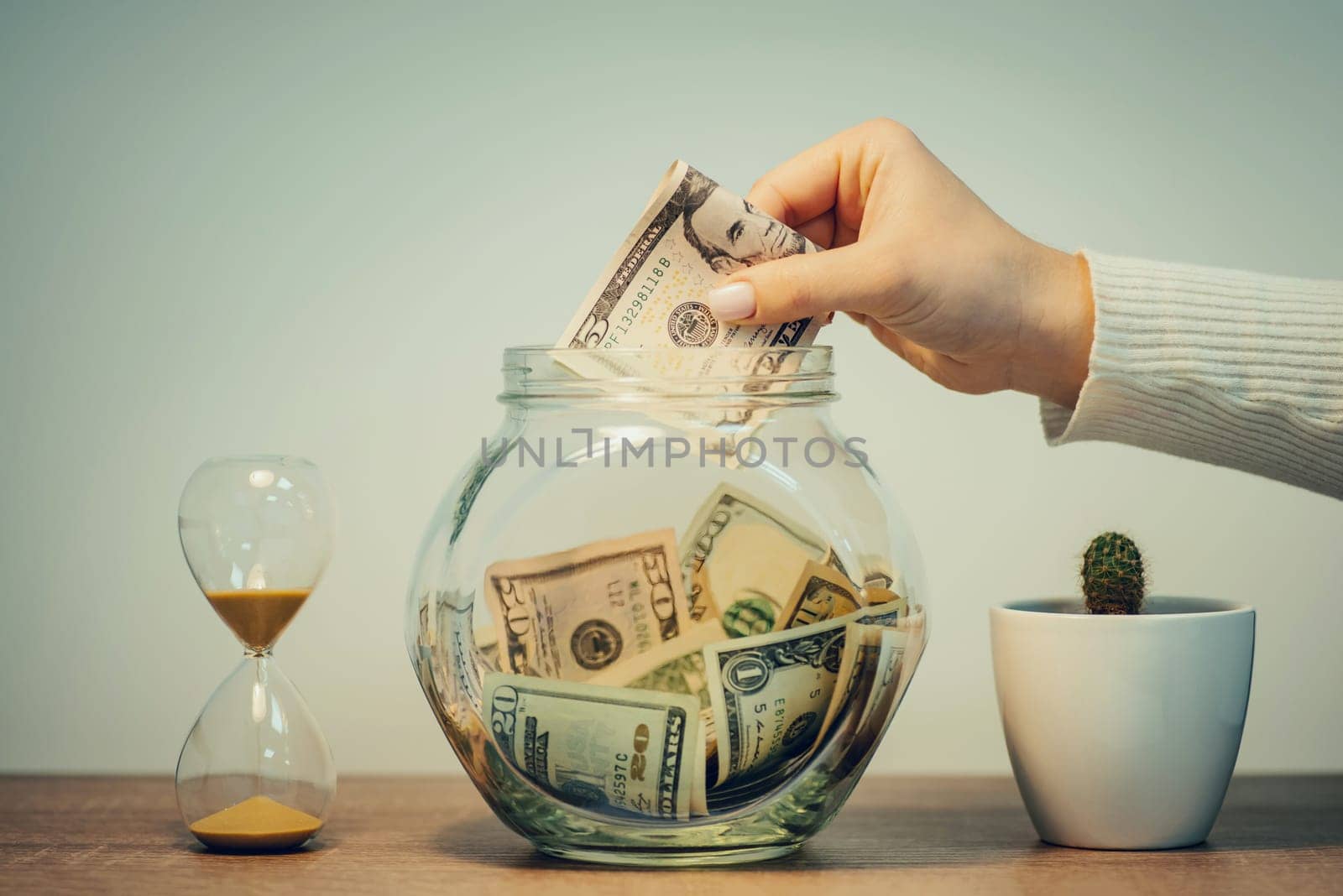 Female hand putting dollars money into glass jar, toned by VitaliiPetrushenko