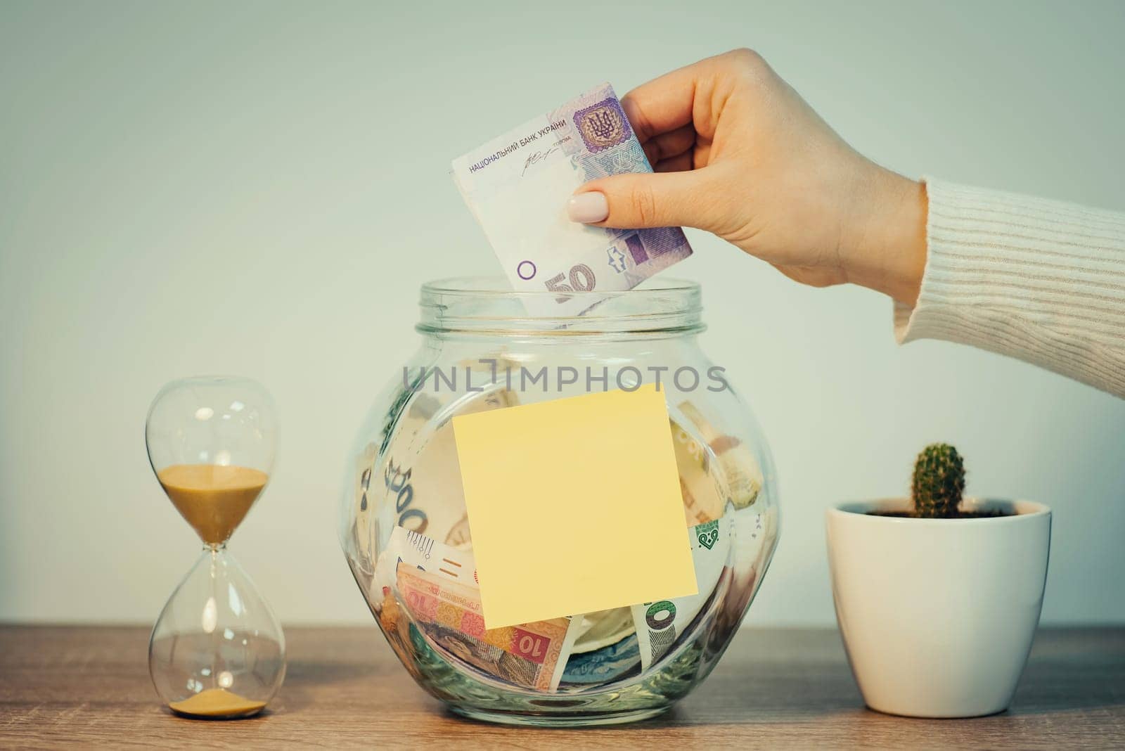 Girl puts 50 hryvnias banknote to the glass jar with blank paper for inscription, toned photo