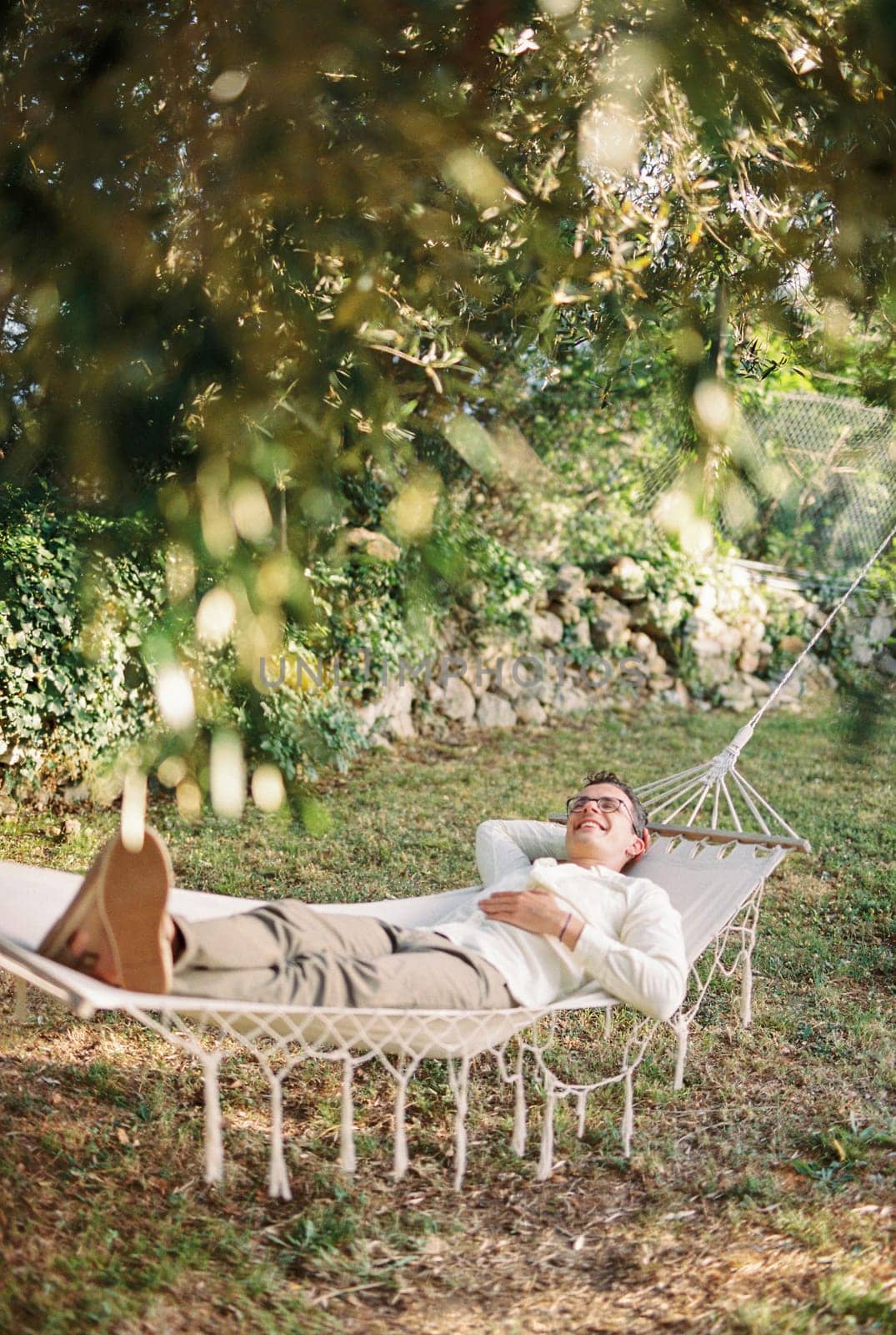 Young smiling man lying in a hammock in a green garden. High quality photo