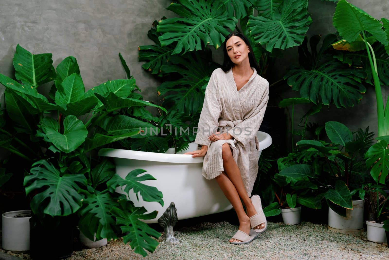 Tropical and exotic spa garden with bathtub in modern hotel or resort with young woman in bathrobe enjoying leisure and wellness lifestyle surrounded by lush greenery foliage background. Blithe