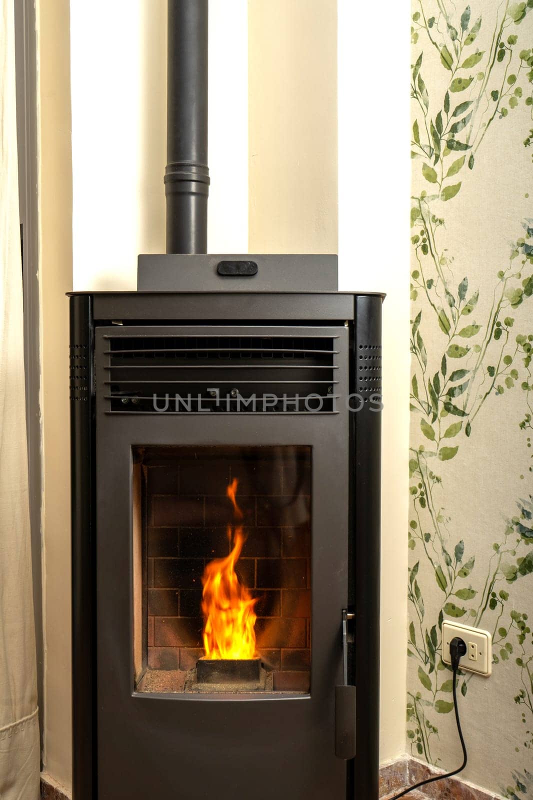Vertical image of a pellet stove with a beautiful flame inside a living room of a house. Renewable energy source. Biomass in pellet form. Green energy