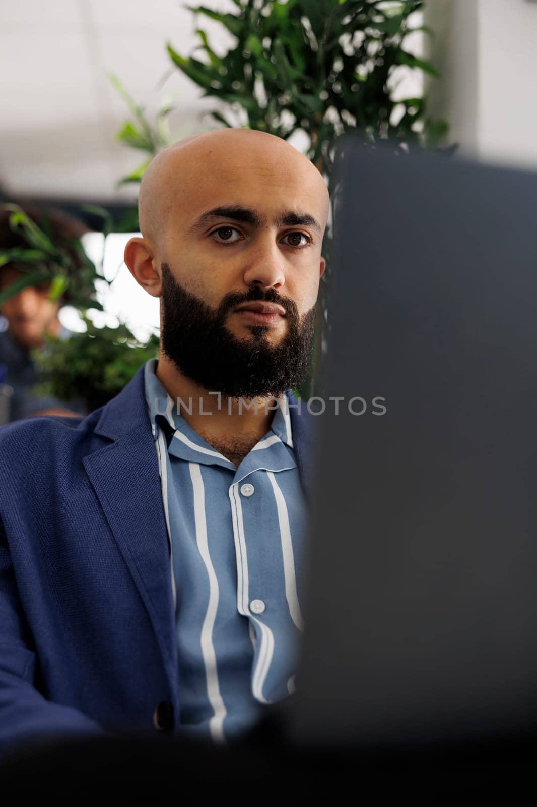 Arab businessman sitting in front of laptop at desk, preparing for video call with clients. Executive manager checking financial analytics report before presentation in coworking space