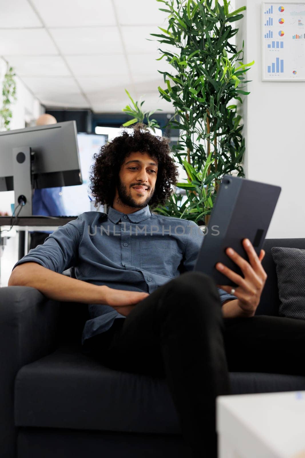 Arab business employee telecommuting, chatting in online meeting using digital tablet. Smiling relaxed start up entrepreneur videconferencing while sitting on couch in office