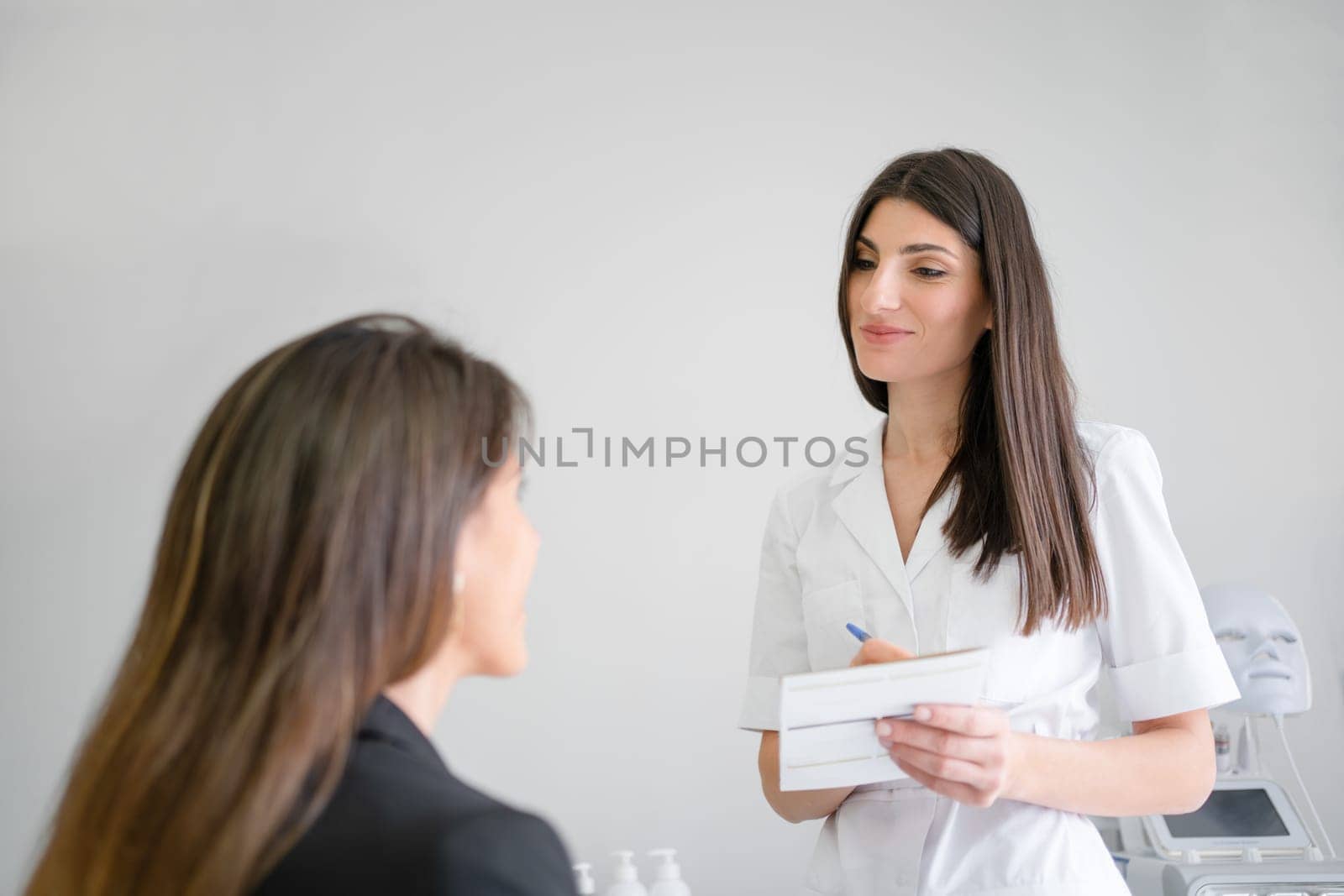 Cosmetologist writing while talking with woman client in beauty clinic by andreonegin