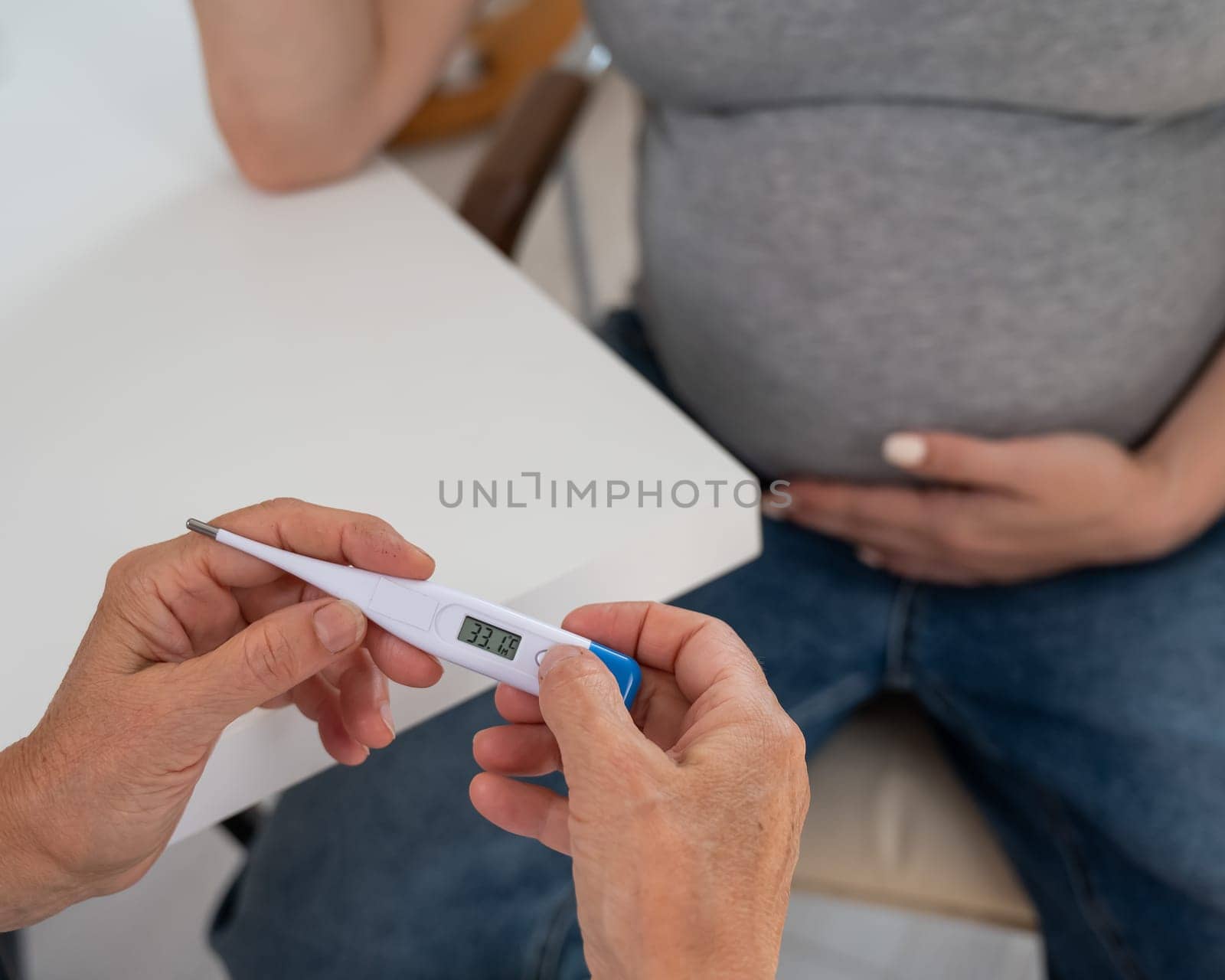 A pregnant woman visits a doctor. Therapist holding an electronic thermometer