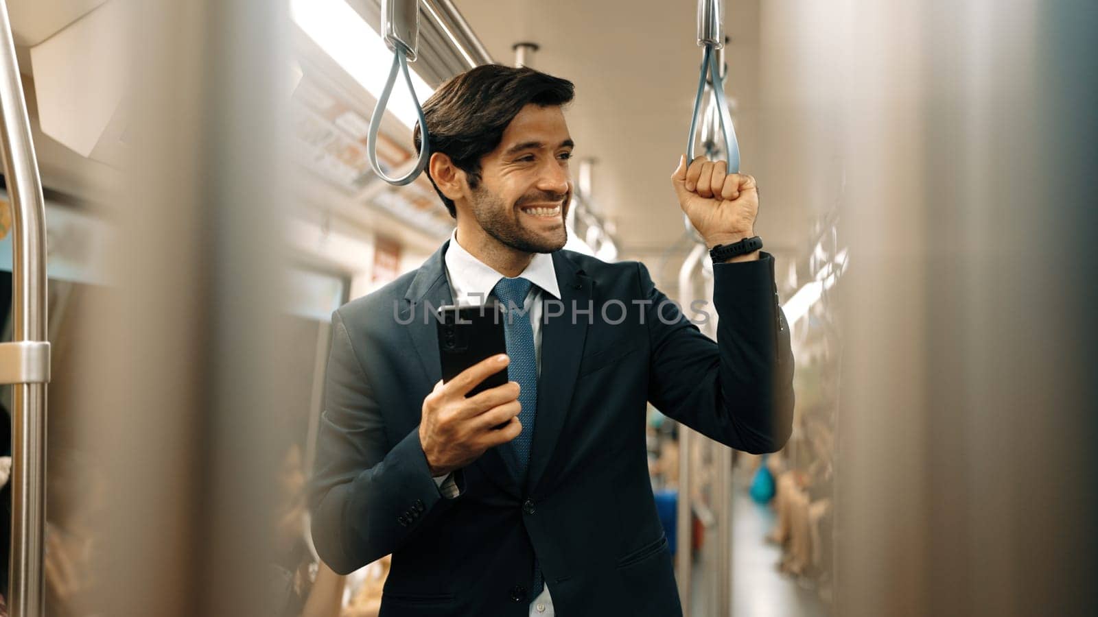 Skilled business man standing in train or subway while holding phone. Professional project manager looking around while enjoy in train ride while playing mobile phone at train station. Exultant.