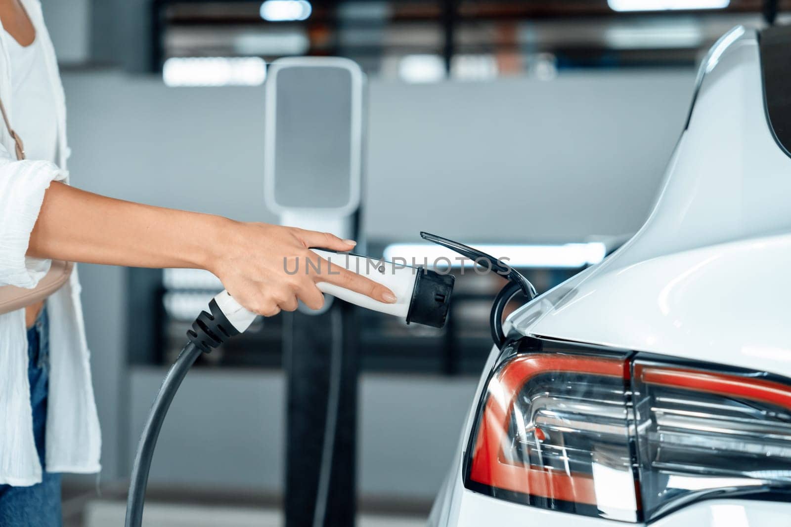 Young woman travel with EV electric car to shopping center parking lot charging in downtown city showing urban sustainability lifestyle by green clean rechargeable energy of electric vehicle innards