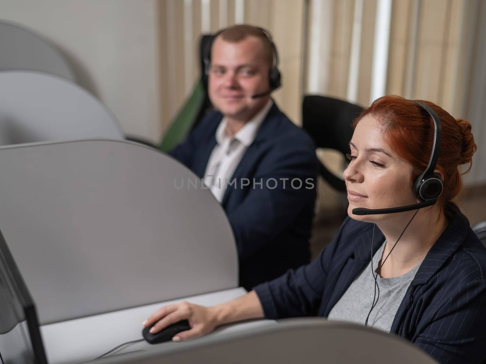 Two friendly call center employees talking to customers. Man and woman working with headsets in office