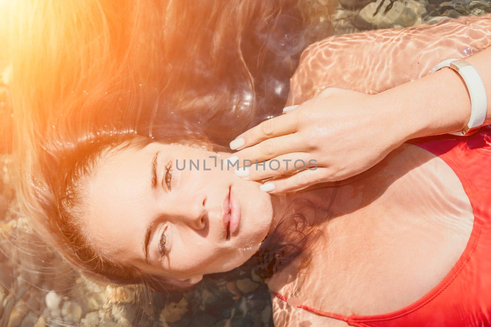 Woman travel portrait. close-up portrait of a happy woman with long hair in a red bikini, floating in water and smiling at the camera. by panophotograph