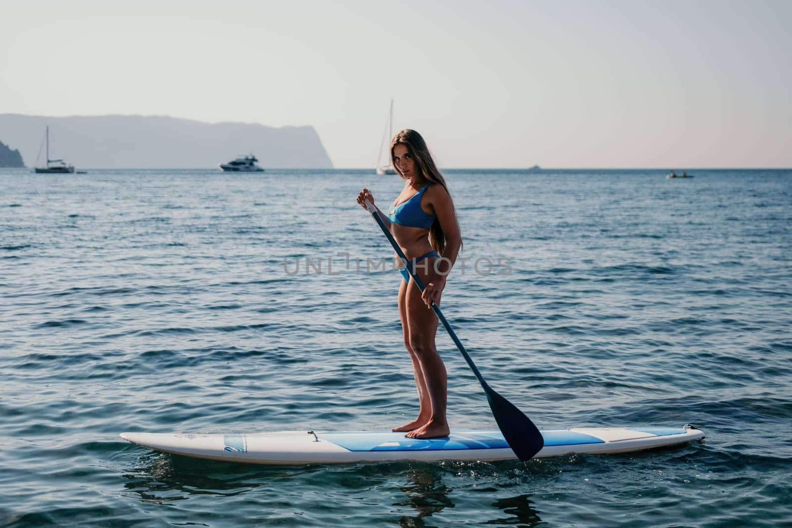 Close up shot of happy young caucasian woman looking at camera and smiling. Cute woman portrait in bikini posing on a volcanic rock high above the sea