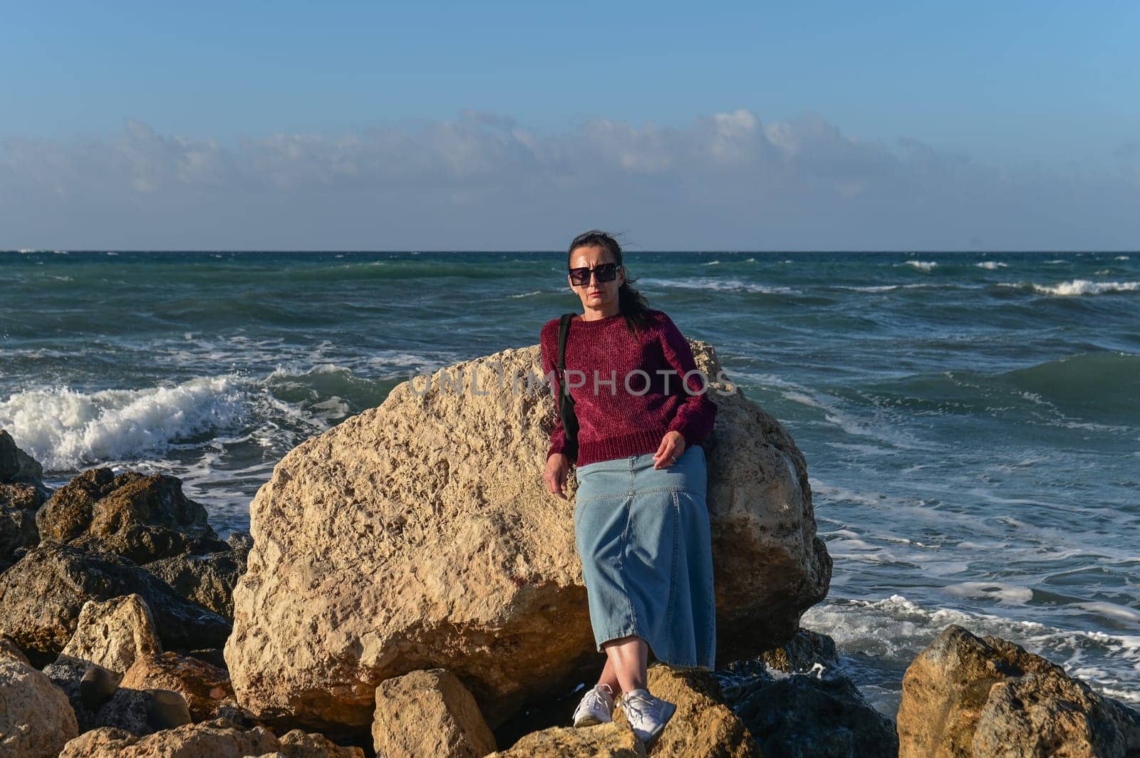 woman in a red jacket against the background of stones and the sea in winter in Cyprus 7