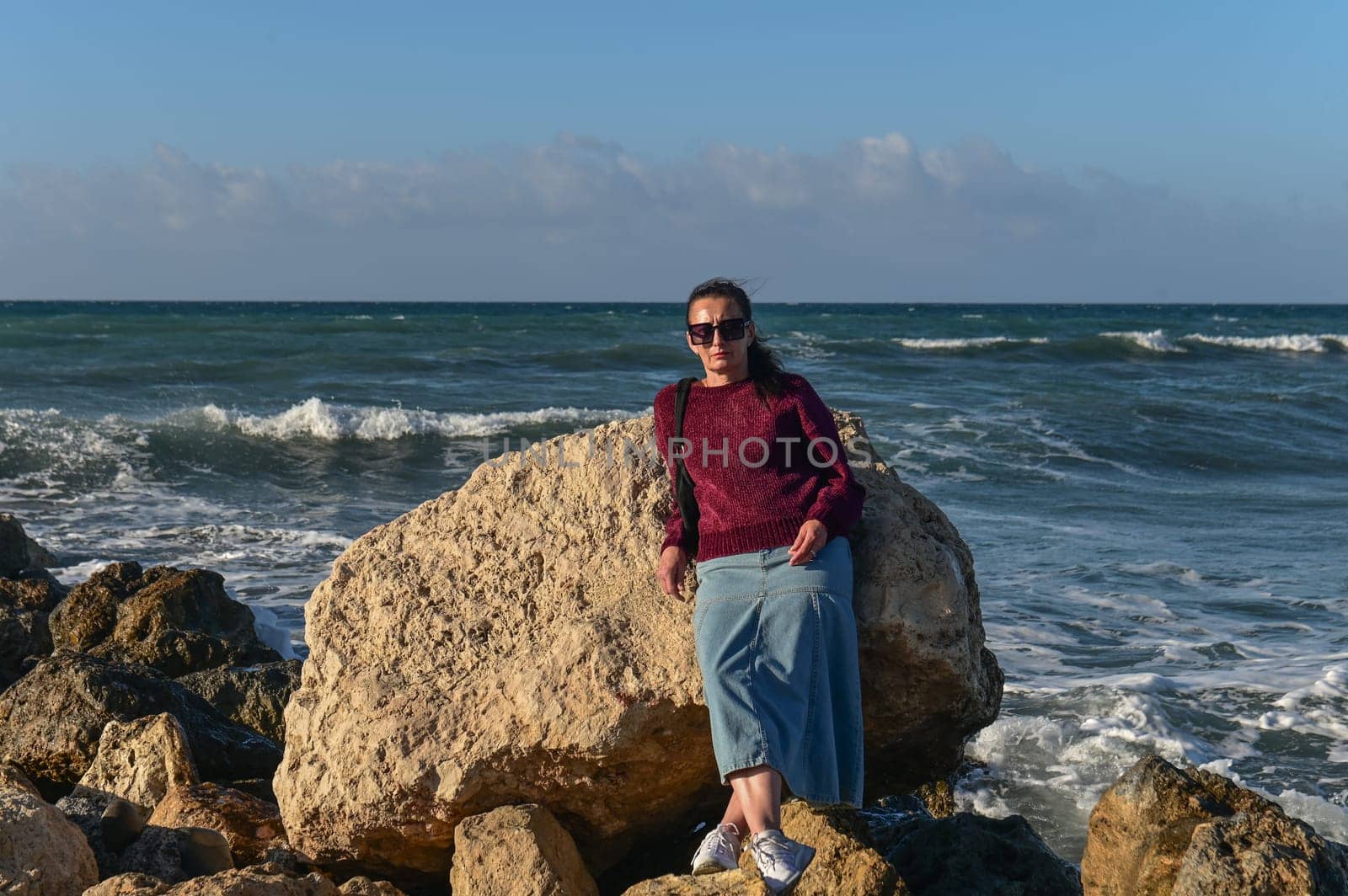 woman in a red jacket against the background of stones and the sea in winter in Cyprus 6