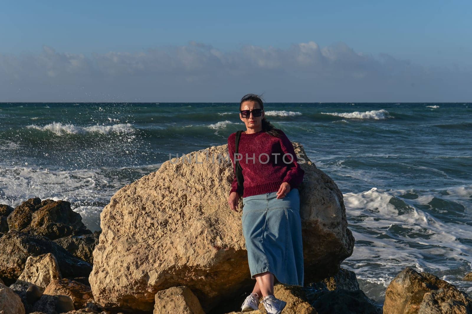 woman in a red jacket against the background of stones and the sea in winter in Cyprus 6 by Mixa74