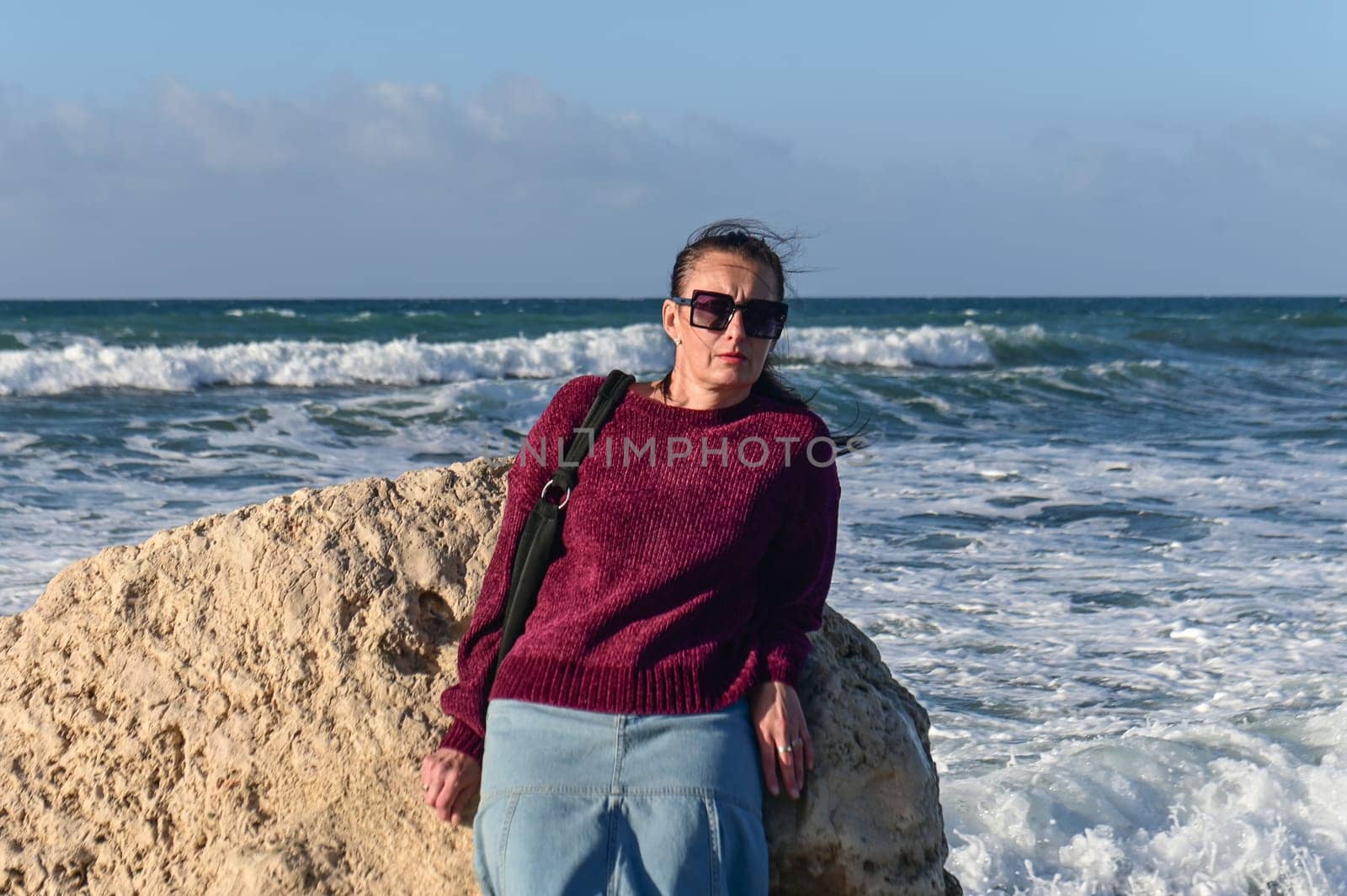 woman in a red jacket against the background of stones and the sea in winter in Cyprus