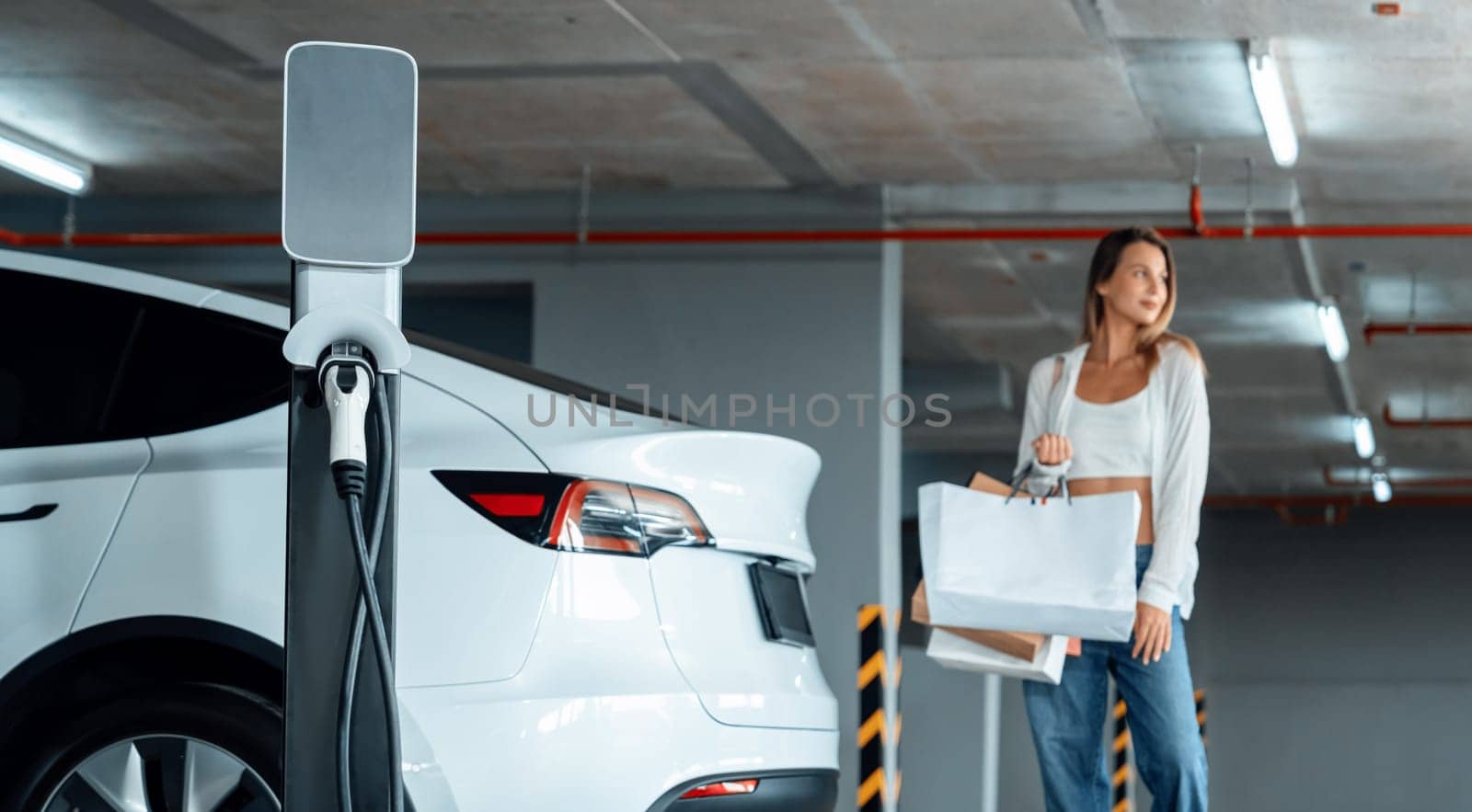 Young woman travel with EV electric car to shopping center parking lot charging in downtown city showing urban sustainability lifestyle by green clean rechargeable energy of electric vehicle innards